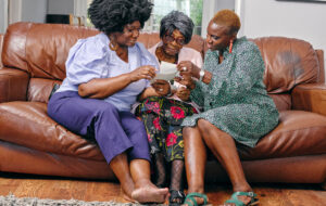 Women And Senior Mother Sitting On Sofa And Looking At Photos